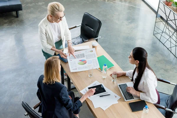 Vista de ángulo alto de las empresarias profesionales que trabajan con dispositivos digitales y gráficos en la oficina - foto de stock