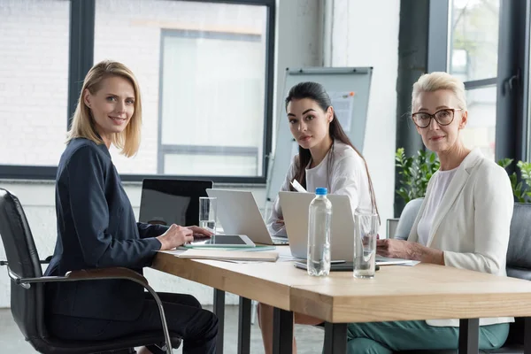 Hermosas empresarias sentadas en la reunión con gadgets en la oficina - foto de stock