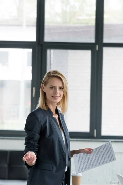 Attractive businesswoman holding documents and gesturing in office — Stock Photo