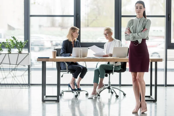 Schöne junge Geschäftsfrau steht mit verschränkten Armen bei einem Treffen im Büro — Stockfoto