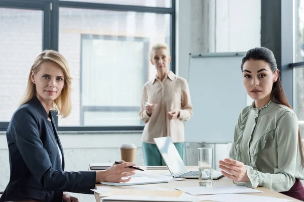 Berufstätige Geschäftsfrauen unterschiedlichen Alters blicken bei Treffen im Büro in die Kamera — Stockfoto