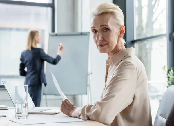 Grauhaarige Geschäftsfrau blickt bei Treffen im Büro in die Kamera — Stockfoto