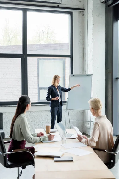 Empresária apresentando projeto em flipchart para colegas em reunião no escritório — Fotografia de Stock