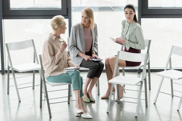 Empresarias profesionales sentadas en sillas y hablando en la oficina - foto de stock