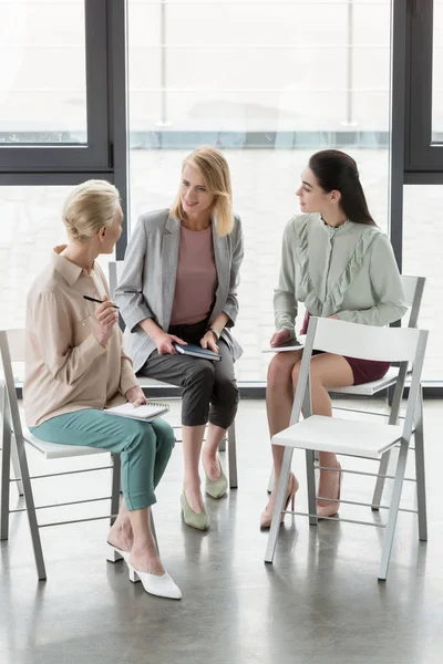 Attractive businesswomen sitting on chairs and talking in office — Stock Photo