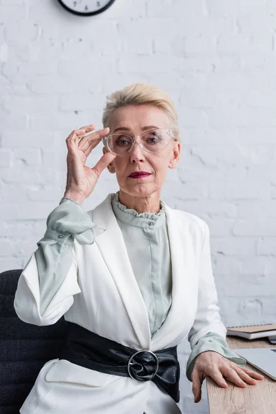 Elegant senior businesswoman in trendy eyeglasses sitting at workplace — Stock Photo