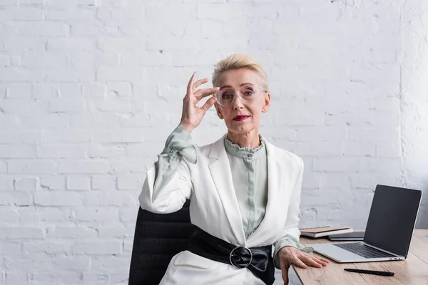 Elegant senior businesswoman in glasses sitting at workplace with laptop — Stock Photo