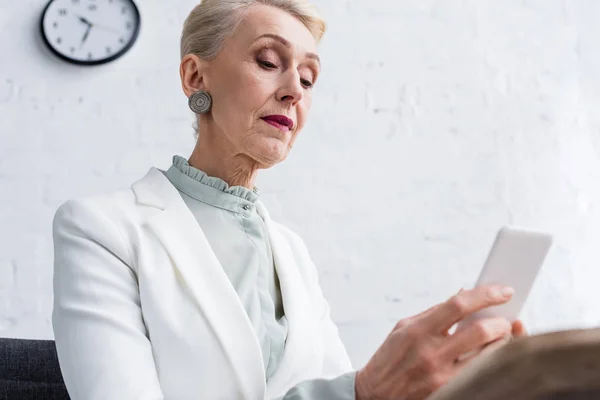 Élégante femme d'affaires senior en utilisant smartphone dans le bureau — Photo de stock