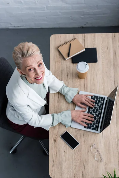 Blick auf lächelnde Seniorin mit Laptop am Arbeitsplatz — Stockfoto