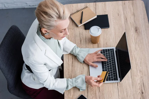 Vista aerea di elegante donna d'affari che utilizza laptop e carta di credito sul posto di lavoro — Foto stock