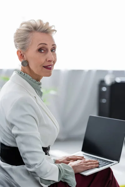 Séduisante femme d'affaires senior utilisant un ordinateur portable avec écran blanc — Photo de stock