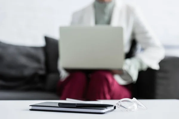 Foyer sélectif de la femme d'affaires à l'aide d'un ordinateur portable, journal, stylo et lunettes couché sur la table au premier plan — Photo de stock