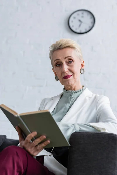 Elegante donna d'affari anziana con libro seduto in ufficio moderno — Foto stock