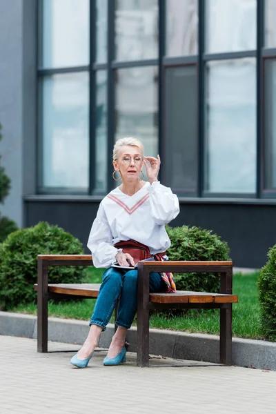 Modische Seniorin mit Tagebuch sitzt auf Bank — Stockfoto