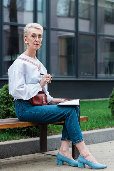 Attractive senior woman in stylish outfit writing in diary — Stock Photo