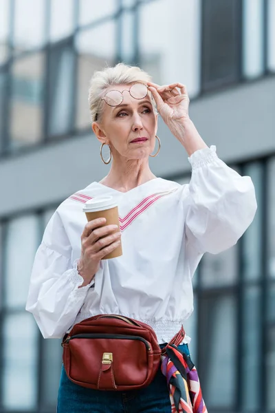 Mujer mayor con estilo en gafas de moda con taza de café desechable - foto de stock