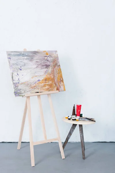 Живопись на станке и краски на стуле в творческой мастерской — стоковое фото