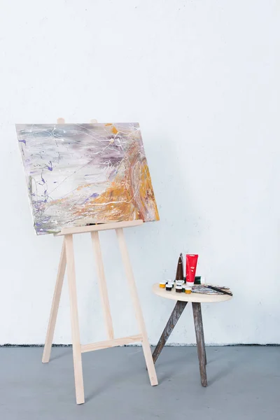 Painting on easel and paints on stool in creative workshop — Stock Photo