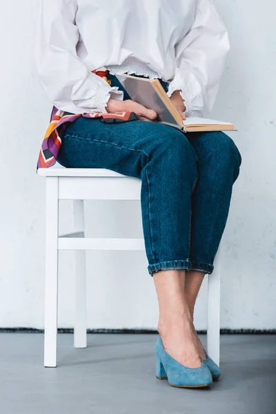 Vista cortada da mulher sentada na cadeira com livro — Fotografia de Stock