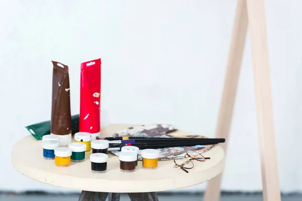 Paintbrushes, palette and paints on stool in artistic workshop — Stock Photo