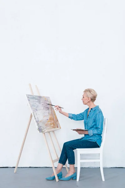 Artista femenina senior pintando con pincel en taller - foto de stock