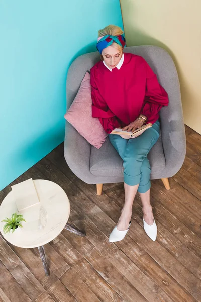 Vista aérea del libro de lectura de la mujer mayor mientras está sentada en el sillón - foto de stock