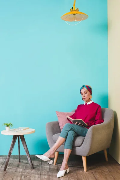 Stylish senior woman reading book while sitting in armchair — Stock Photo