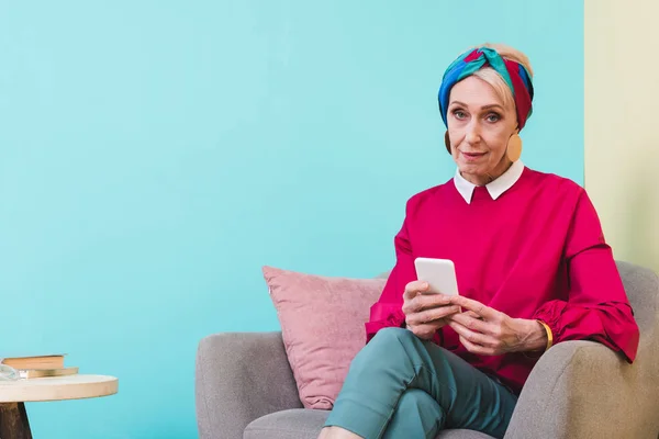 Donna anziana utilizzando smartphone mentre seduto in poltrona — Foto stock