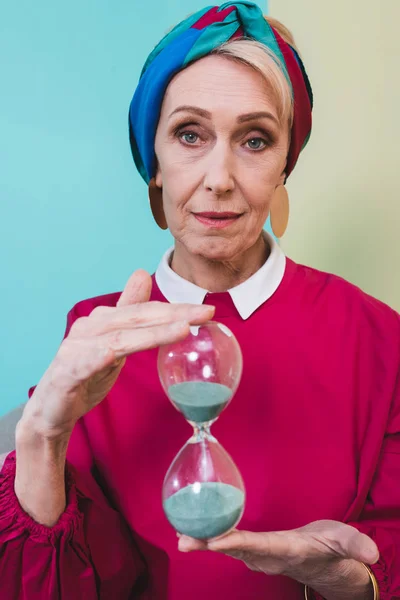 Красивая пожилая женщина держит песочные часы с голубым песком — стоковое фото