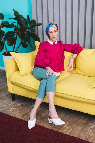 Beautiful senior woman sitting on yellow sofa — Stock Photo