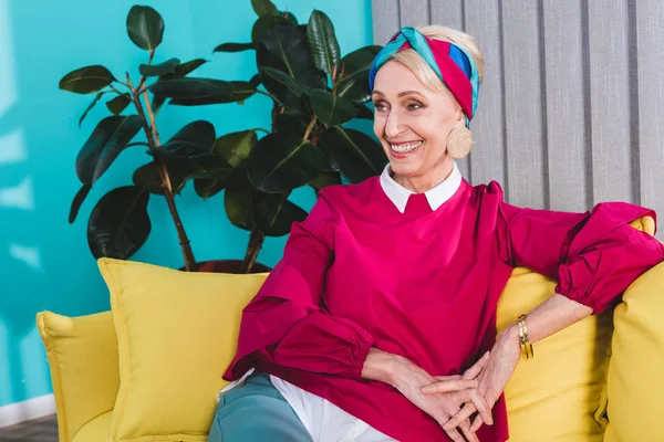 Lächelnde, stylische Seniorin auf gelbem Sofa — Stockfoto
