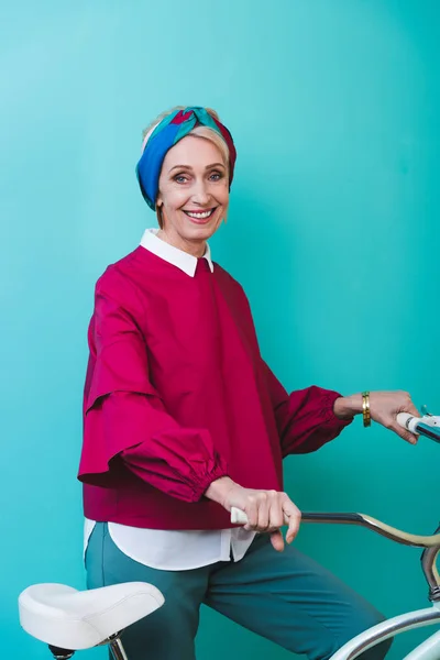 Fröhliche Seniorin steht mit Fahrrad auf Türkis — Stockfoto