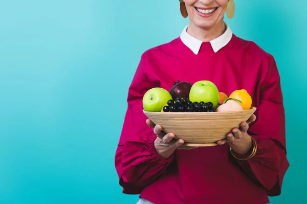 Cropped view of smiling senior woman with fresh fruits, isolated on blue — Stock Photo