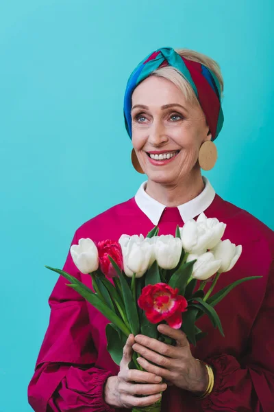 Séduisante femme âgée souriante avec bouquet de fleurs printanières, isolée sur turquoise — Photo de stock