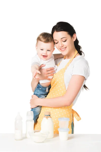 Счастливая мать в фартуке держа мальчика за столом с детьми питание изолированы на белом фоне — стоковое фото