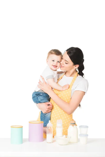Mother with little son in hands at table with children food and milk isolated on white background — Stock Photo