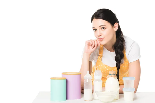 Улыбающаяся молодая женщина в фартуке за столом с детским питанием и молоком на белом фоне — стоковое фото