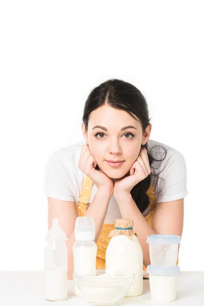 Young woman in apron standing at table with milk, bowl, plastic containers and baby bottles — Stock Photo