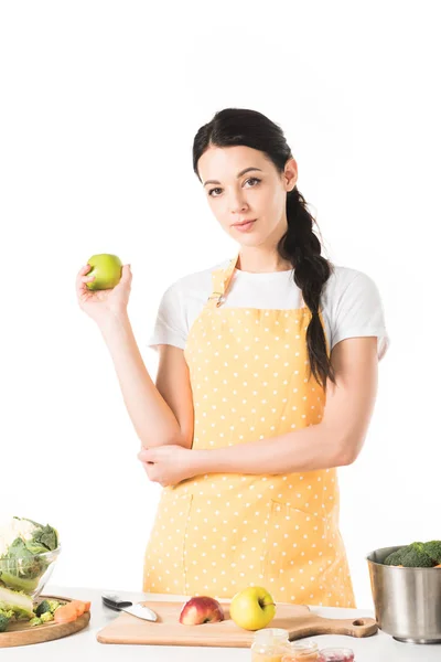 Mulher segurando maçã perto da mesa com tábua de corte, panela, maçãs e legumes — Fotografia de Stock