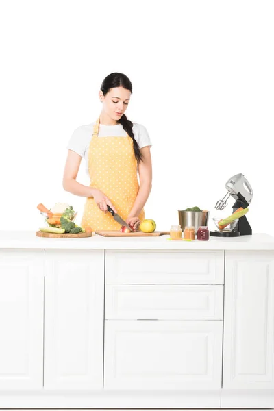 Femme dans tablier coupe pomme à table avec mélangeur, casserole, pots, fruits et légumes — Photo de stock