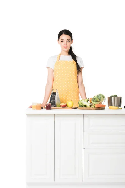Junge Frau in Schürze steht an einer Tischplatte mit Obst und Gemüse isoliert auf weißem Hintergrund — Stockfoto
