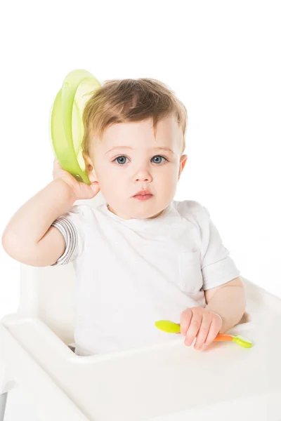 Baby boy sitting in highchair with plate and spoon isolated on white background — Stock Photo