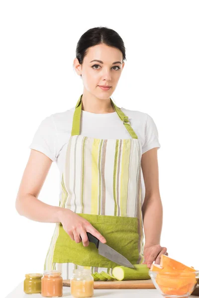 Jeune femme en tablier de coupe de courgettes par couteau isolé sur fond blanc — Photo de stock