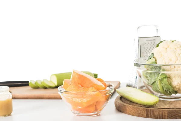 Closeup shot of bowl with pumpkin slices, zucchinis, cutting boards, grater and bowl with cauliflower isolated on table — Stock Photo