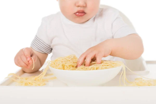 Cropped shot of baby boy eating spaghetti by hands and sitting in highchair — Stock Photo