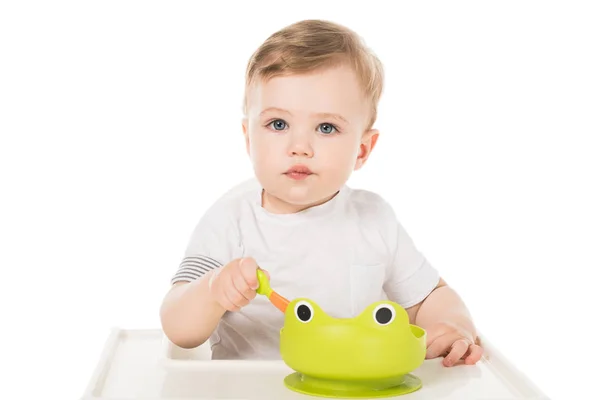 Очаровательный маленький мальчик ест из тарелки в виде лягушки и сидит в кресле — стоковое фото