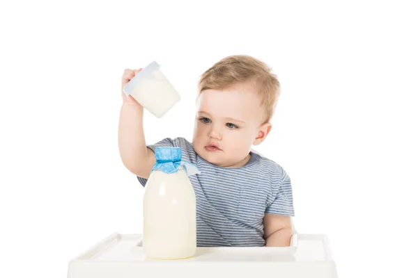 Niño pequeño con contenedor de plástico y botella de leche y sentado en trona aislado sobre fondo blanco - foto de stock