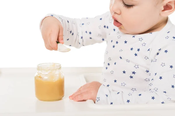 Bebé niño comiendo puré de tarro y sentado en trona aislado sobre fondo blanco - foto de stock