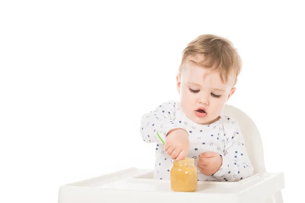 Little boy eating puree from jar and sitting in highchair isolated on white background — Stock Photo
