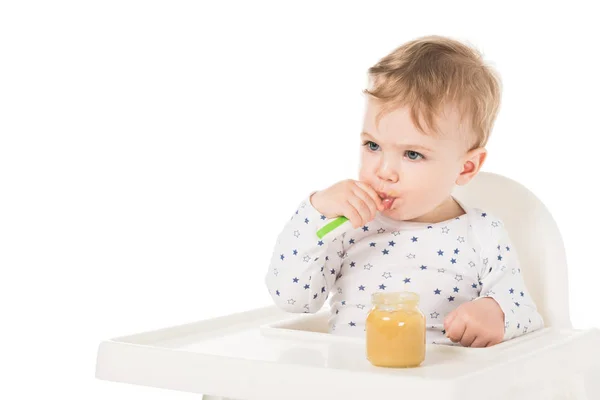Bambino mangiare purea da vaso e seduto in seggiolone isolato su sfondo bianco — Foto stock